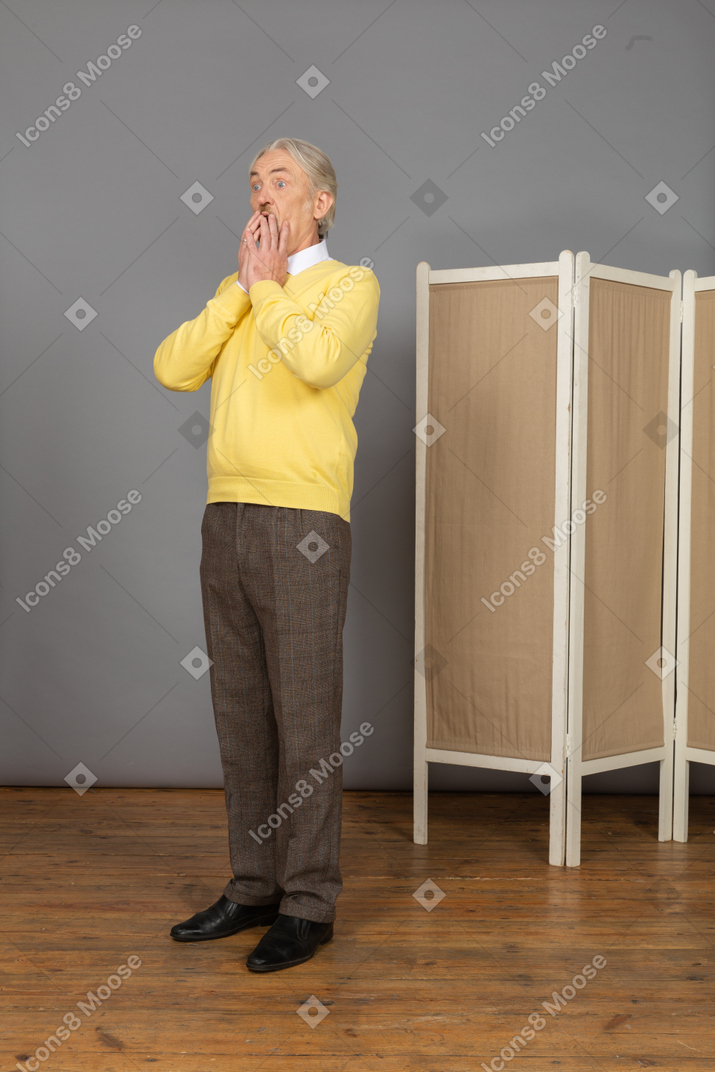 Vista de tres cuartos de un anciano sorprendido tocando la boca