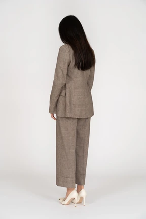 Three-quarter back view of a young lady in brown business suit looking down