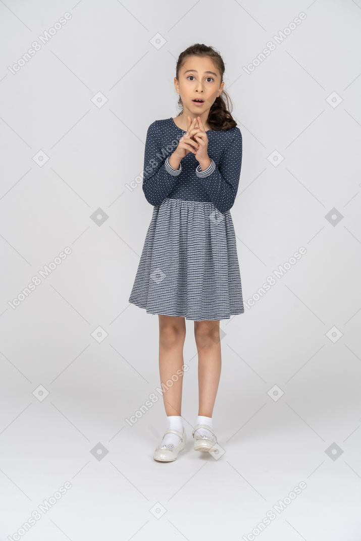 Vista frontal de una niña jugando con sus dedos nerviosamente mirando consternada