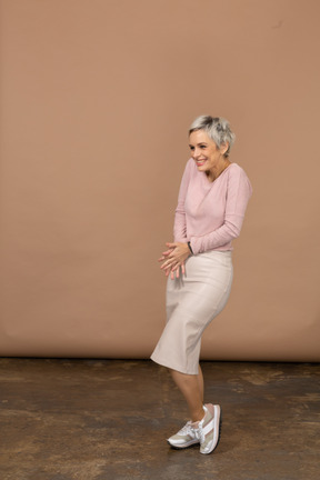 Vista lateral de uma mulher feliz em roupas casuais, posando em uma perna