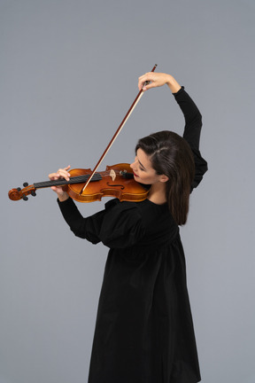 Close-up de uma jovem alegre de vestido preto tocando violino