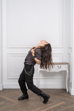 Vista lateral de una mujer rockera rasgando su camiseta mientras echa la cabeza hacia atrás