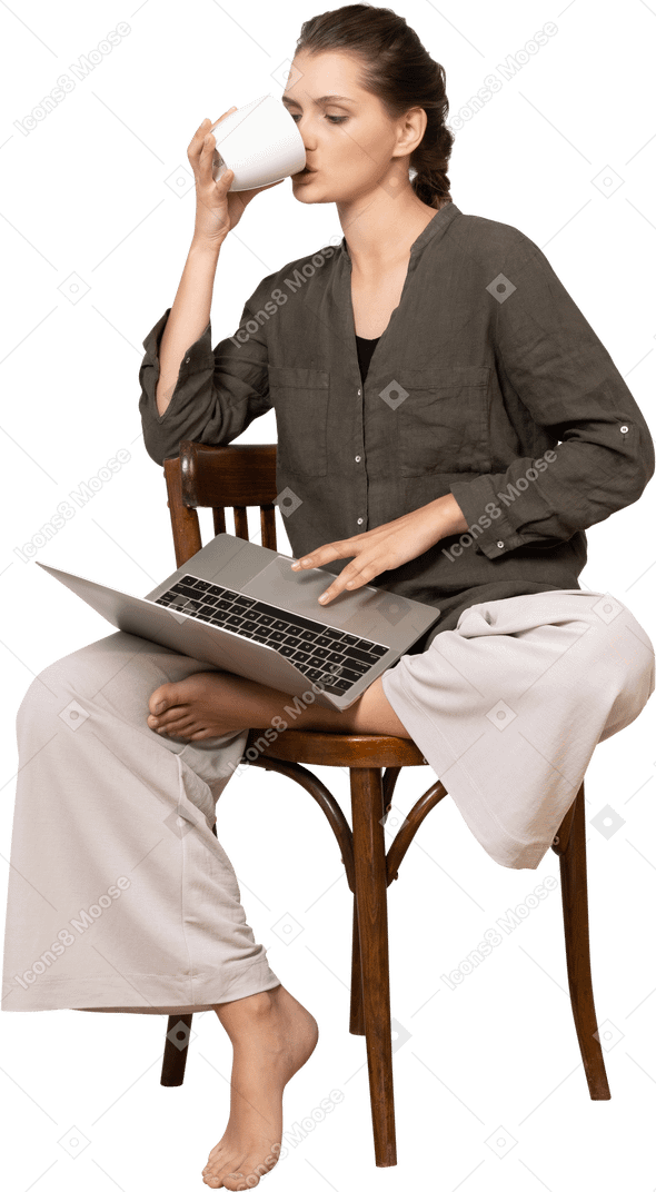 一位穿着家居服的年轻女子坐在椅子上，拿着笔记本电脑喝咖啡的前视图