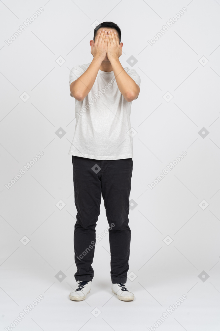 Front view of a man in casual clothes covering face with hands