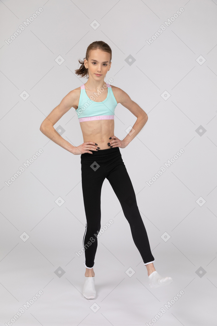 一个年轻的女孩，穿着运动服，将手放在臀部上，抬起腿的前视图