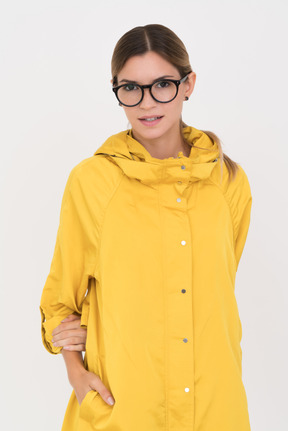 Girl in yellow coat and glasses with one hand holding another one kidden in the pocket