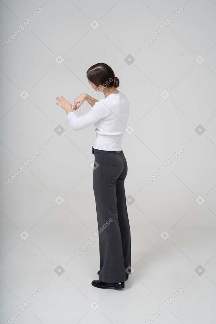 Side view of a woman in black pants and white blouse looking at her hand