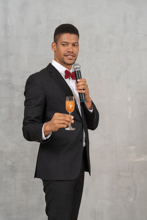 Young man with a mic and glass of champagne looking aside