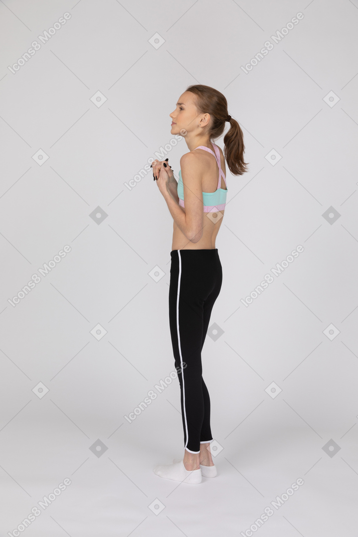Three-quarter back view of a hopeful teen girl in sportswear holding hands together