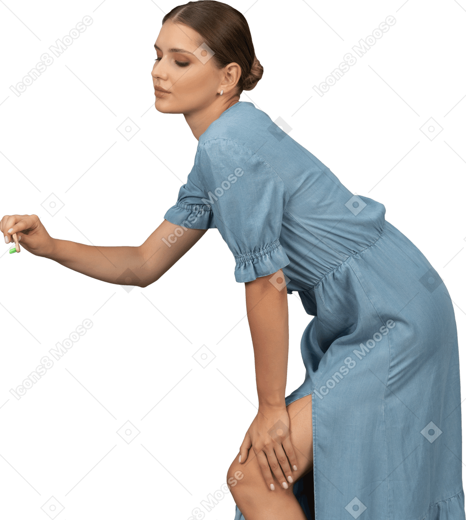 Вид сбоку молодой женщины в синем платье, держащей зубную щетку и наклонившейся вперед