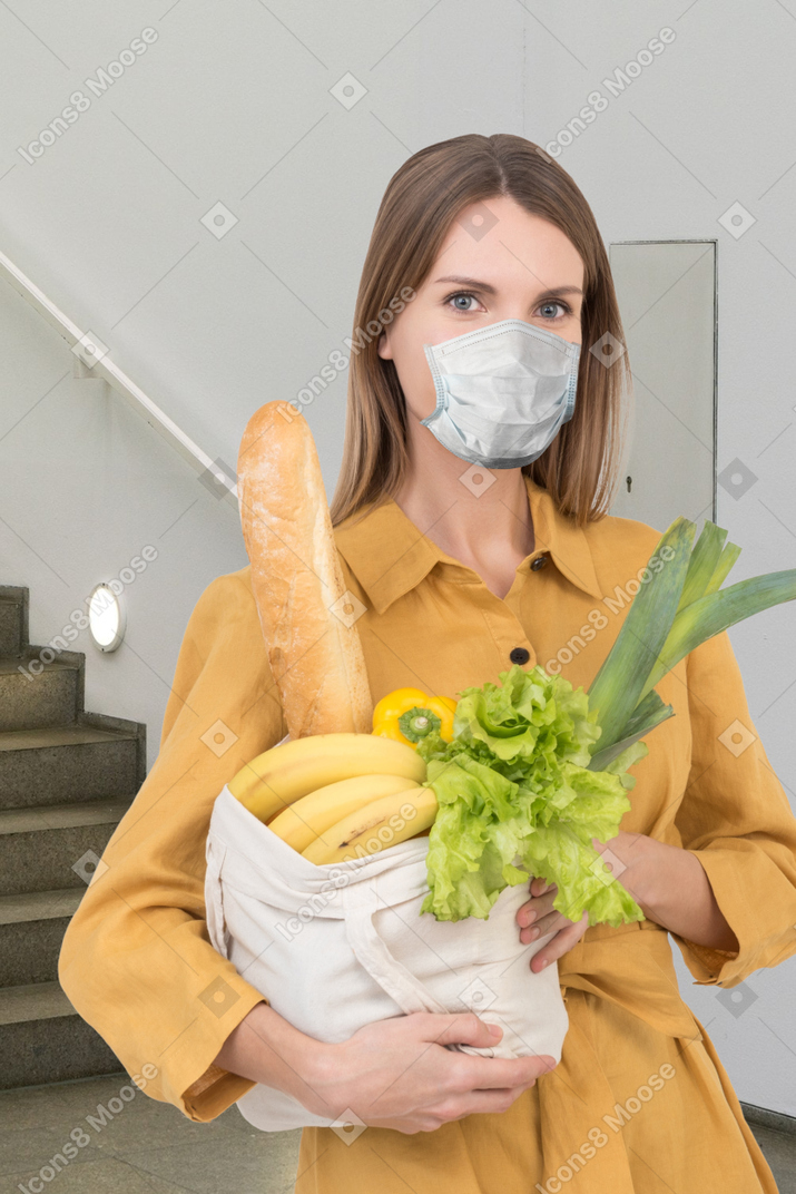 A woman wearing a face mask holding a basket of food