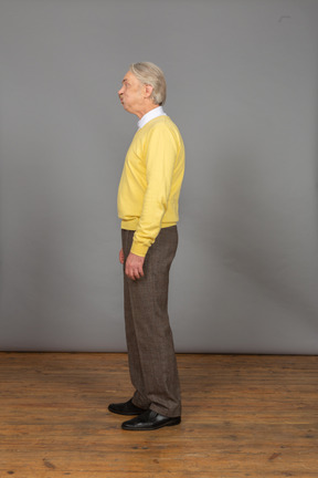 Seitenansicht eines alten schmollenden mannes im gelben pullover, der beiseite schaut und verzieht das gesicht