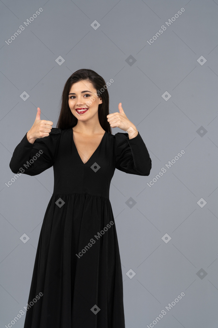 Vista frontale di una giovane donna in un abito nero che mostra i pollici in su