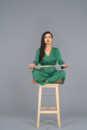 A figura intera di una giovane donna che tiene il suo clarinetto sulle ginocchia mentre è seduta su una sedia di legno