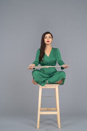 Full-length of a young lady holding her clarinet on her knees while sitting on a wooden chair