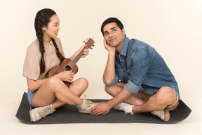 Young asian woman playing her guitar and young man is enchanted by her