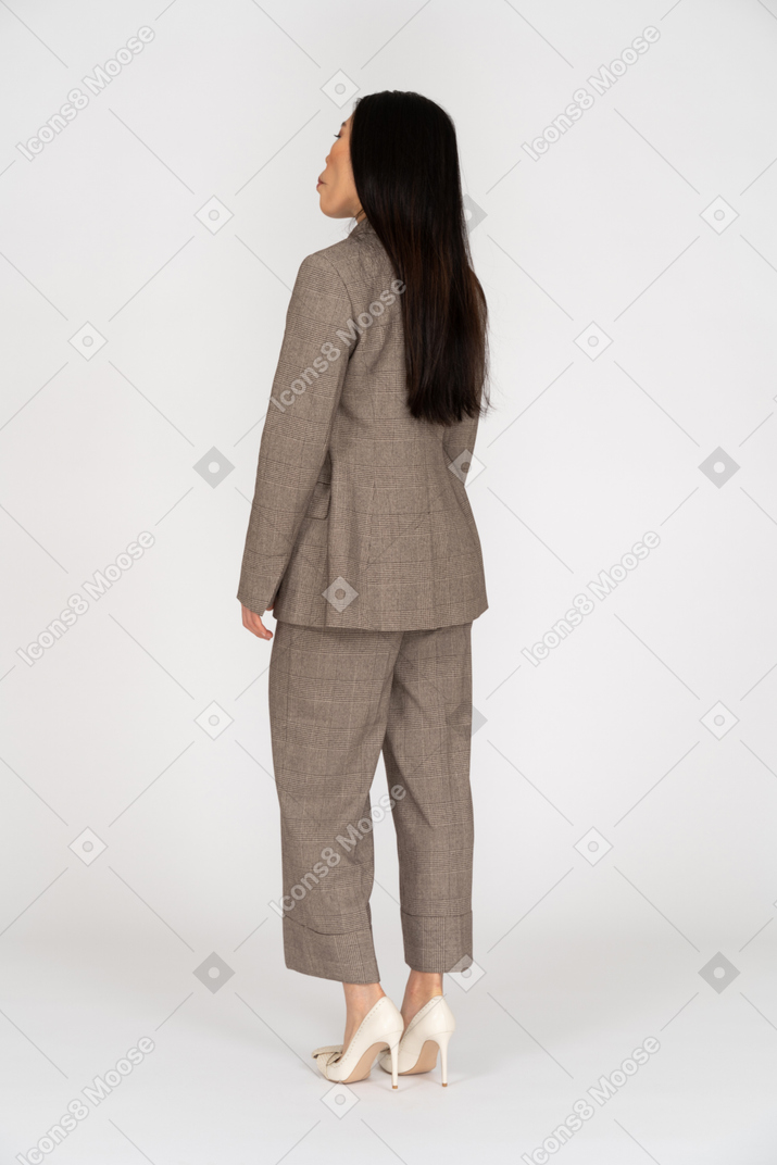 Three-quarter back view of a young lady in brown business suit drawing in her cheeks