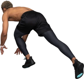 Three-quarter back view of a shirtless dark-skinned sprinter ready to run