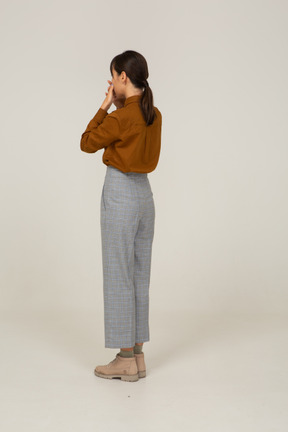 Three-quarter back view of a young asian female in breeches and blouse touching her face