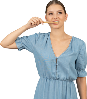 彼女の歯を磨く青いドレスを着た若い女性の正面図