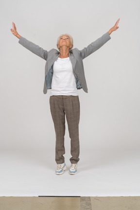 Vista frontal de una anciana en traje de pie sobre los dedos de los pies y levantando los brazos