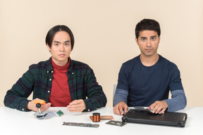 Two young geeks sitting at the table and fixing laptop