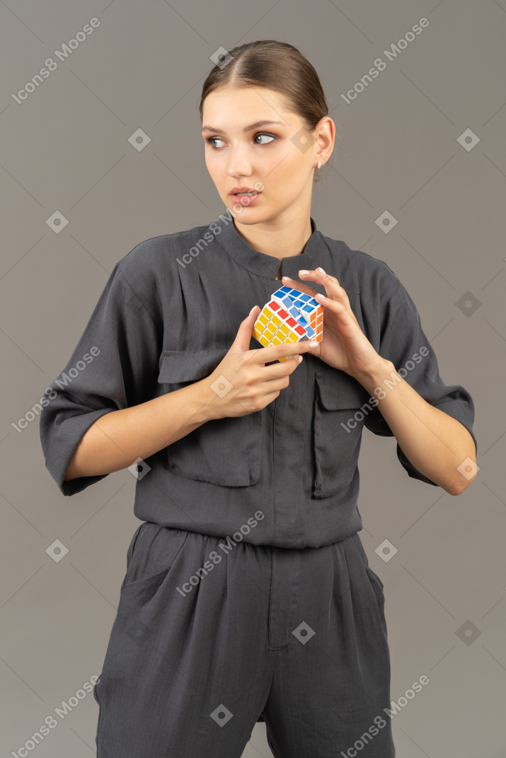 Вид спереди молодой женщины в комбинезоне, держащей кубик рубика