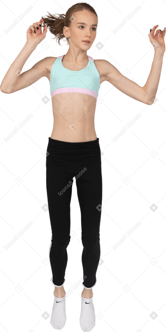 Vue de face d'une adolescente en tenue de sport en levant les mains en sautant