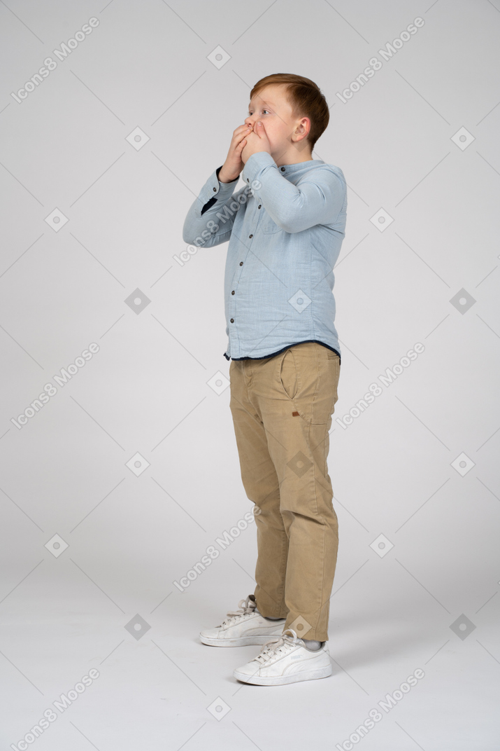 Side view of a scared boy covering mouth with hands