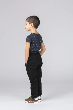 Side view of a cute boy posing with hands in pockets and making faces