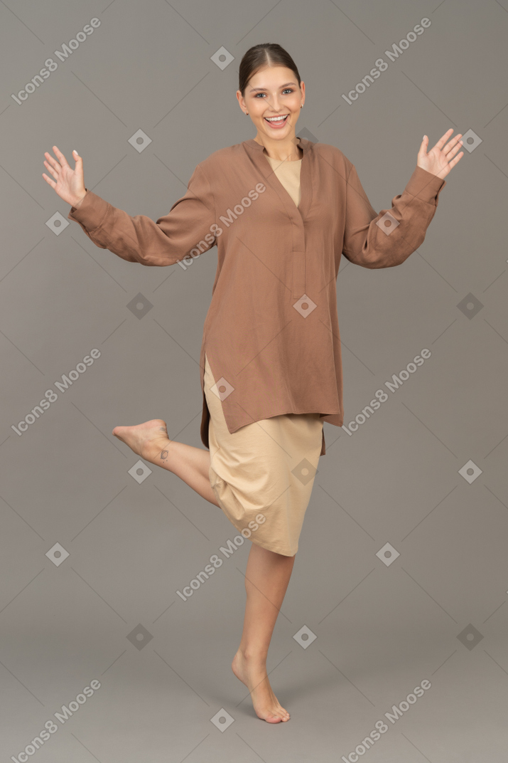 Cheerful young woman standing barefoot on tiptoe with lifted arms