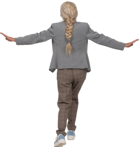 Rear view of an old lady in suit balancing on one leg and outstretching arms