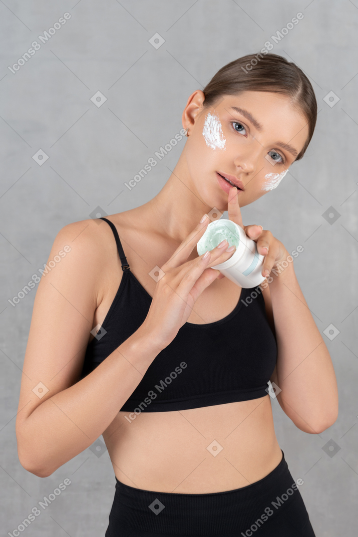 Beautiful woman applying moisturizing cream on her face