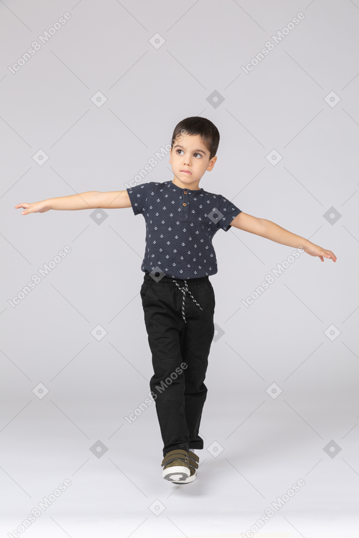 Vista frontal de um menino fofo se equilibrando em uma perna e estendendo os braços