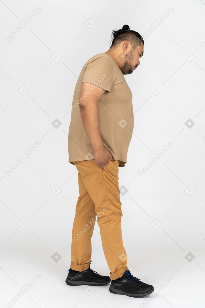Thoughtful asian man standing in profile with hands in pockets