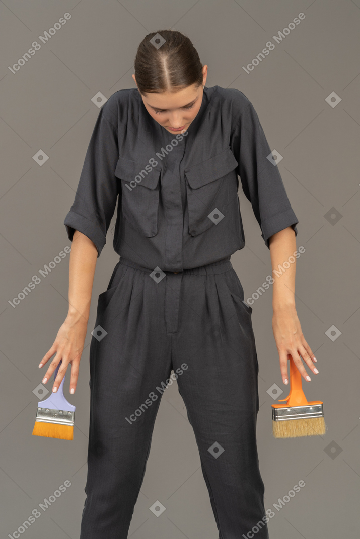 Woman in gray coveralls holding paint brushes
