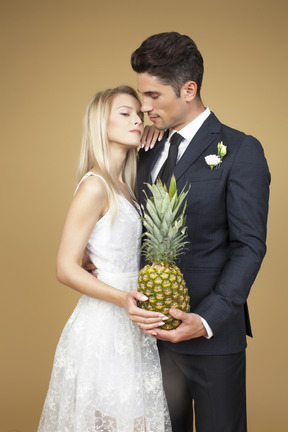 Bride and groom standing shoulder to shoulder and holding a pineapple