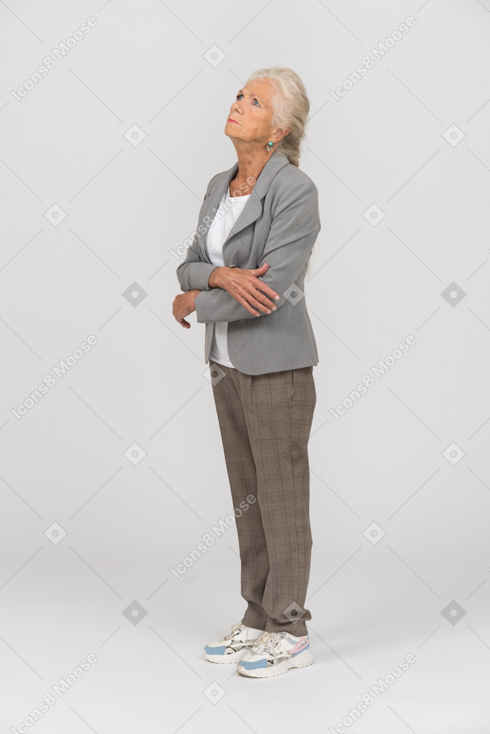 一位身穿西装的老妇人双臂交叉站立，抬头仰望的侧视图