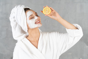 Close-up of a smiling woman in bathrobe holding a lemon