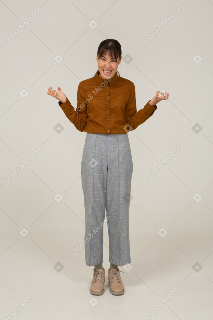 Вид спереди молодой злой азиатской женщины в бриджах и блузке, сжимающей зубы и кулаки