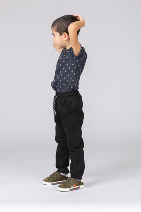 Vista lateral de um lindo menino posando com as mãos atrás da cabeça