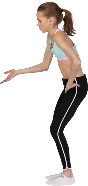Vista lateral de uma adolescente em roupas esportivas apontando as mãos em algum lugar para baixo