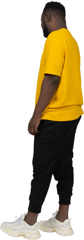 静止している黄色のtシャツを着た若い浅黒い肌の男の4分の3の背面図