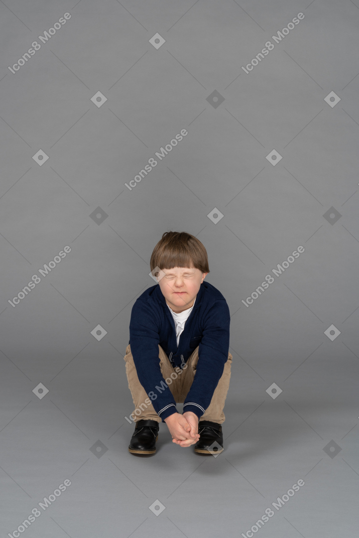 Little boy squatting with eyes shut, looking afraid