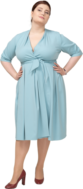 Вид спереди женщины в синем платье позирует с руками на бедрах