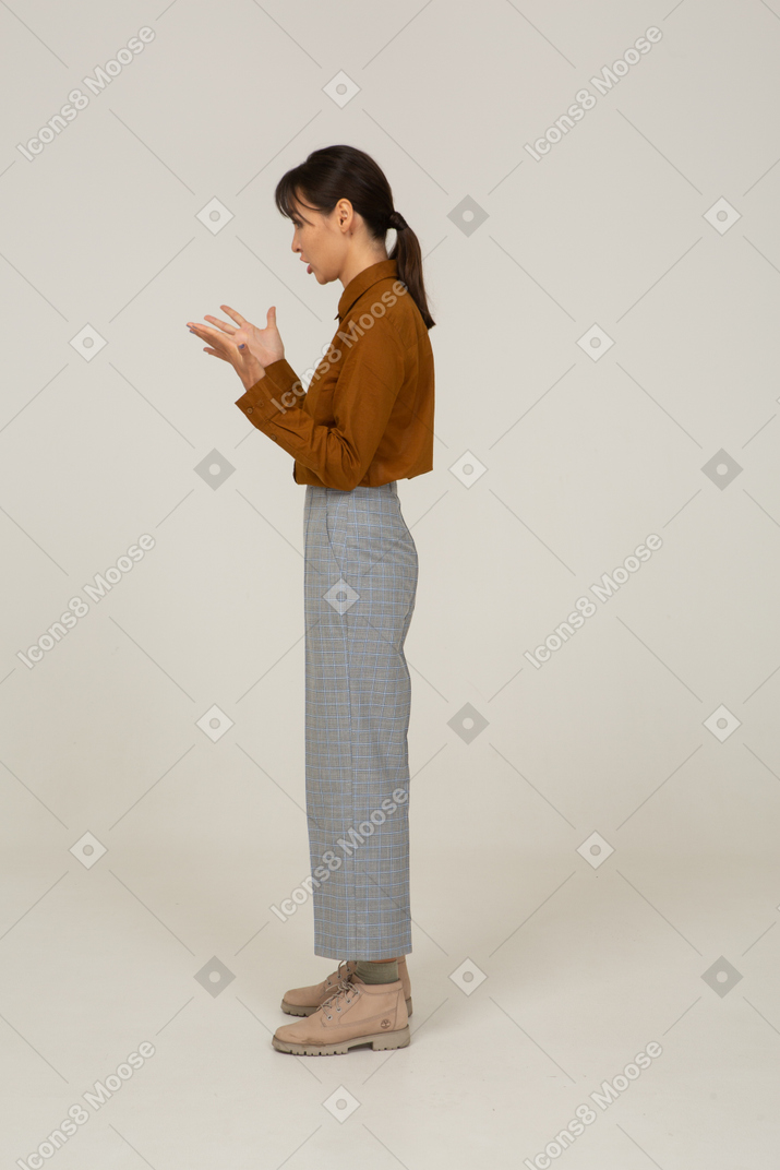 Vista laterale di un interrogatorio giovane donna asiatica in calzoni e camicetta alzando le mani