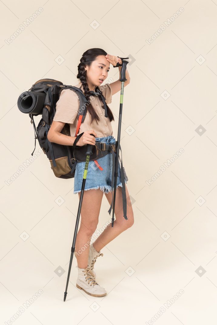 Tired hiker woman walking using trekking poles and drying her forehead with hand