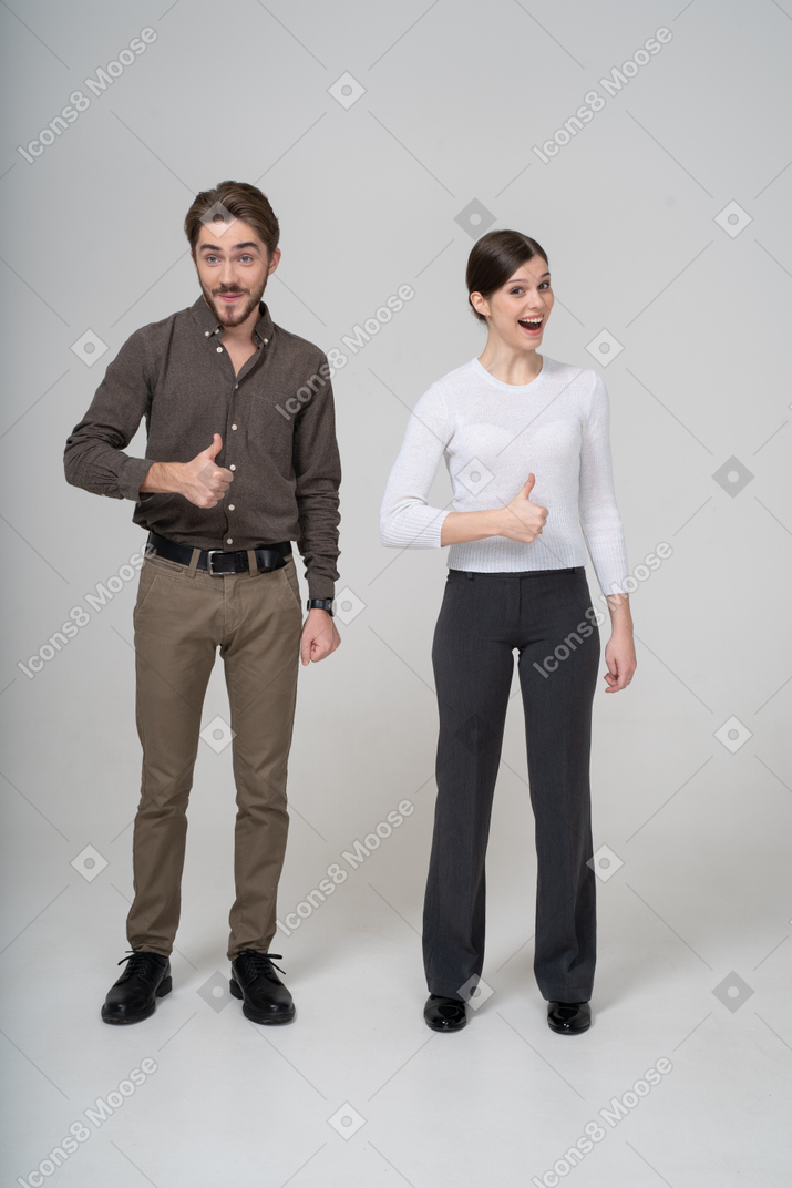 Vista frontal de una joven pareja alegre en ropa de oficina mostrando el pulgar hacia arriba