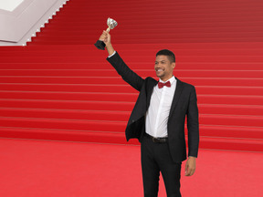 A man in a tuxedo holding up a trophy on a red carpet