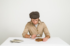 Handsome young investigator looking on wooden box through magnifying glass